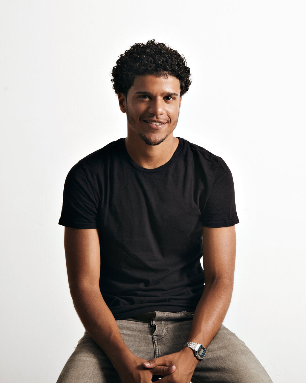 Man wearing a black t-shirt and gray pants sitting on a white background